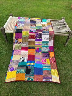 a patchwork quilt sitting on top of a wooden bench in the middle of a field