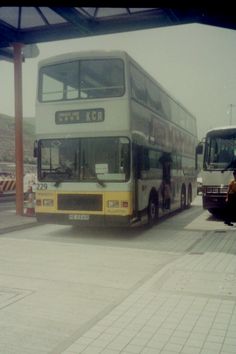 two double decker buses parked next to each other on the side of the road in front of a bus stop