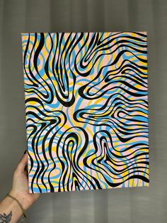 a person holding up a colorful art piece in front of a gray background with black, yellow, and blue swirls on it