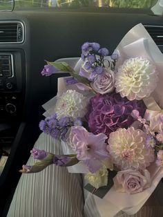 a bouquet of purple and white flowers sitting in the passenger seat of a car,