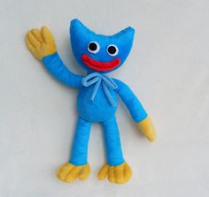 a blue stuffed animal with yellow feet on a white tablecloth background and one hand up in the air