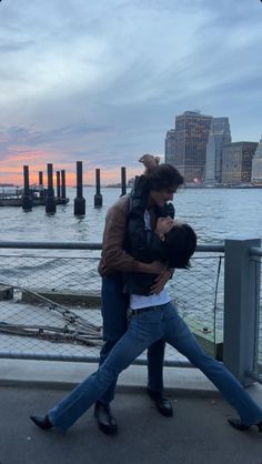 a man and woman walking on the sidewalk next to water with buildings in the background