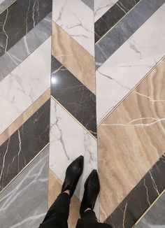 a person wearing black shoes standing in front of a marble floor with gold and grey stripes