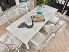 a dining room table with white chairs and a book on top of it, in front of a fireplace