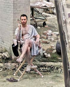 a man sitting on top of a wooden chair next to a brick wall holding an umbrella