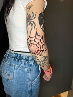 a woman with a spider web tattoo on her arm and shoulder, standing in front of a wall