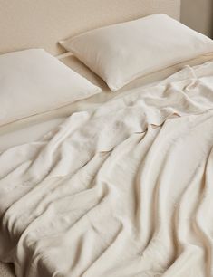 an unmade bed with white sheets and pillows