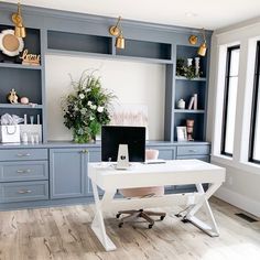 a desk with a laptop on top of it in front of some shelves and windows