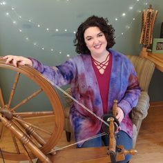 a woman sitting in front of a spinning wheel with her hands on the spokes