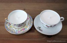 two tea cups and saucers with a lit candle in them on a wooden table