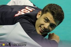 a man laying on top of a tennis court next to a blue wall and smiling