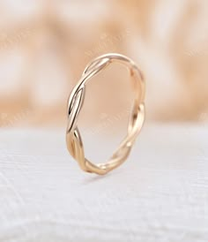 a gold wedding ring with twisted design on it's side, sitting on a white surface