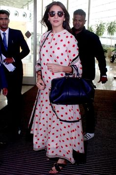 a woman in a white and red dress is carrying a black handbag while walking through an airport