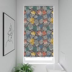 a bathroom with a toilet, sink and window covered in colorful leaves print roller shades