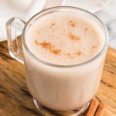 a glass mug filled with milk and cinnamon on top of a wooden cutting board