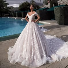 a woman standing in front of a pool wearing a wedding dress with flowers on it