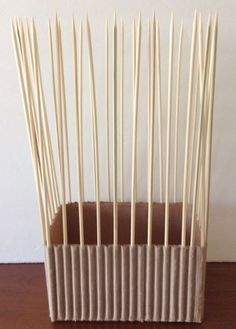 several sticks sticking out of a cardboard box on a table with a white wall in the background