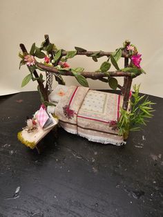 a bed made out of branches and flowers on top of a black table next to a potted plant