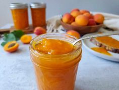 a glass jar filled with orange jam sitting on top of a table next to bowls of fruit