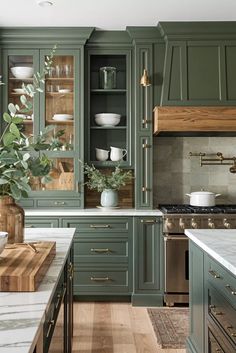 a kitchen with green cabinets and marble counter tops, wooden flooring and brass pulls