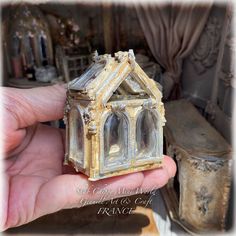 a hand is holding a miniature house made out of glass and gold leafy paint