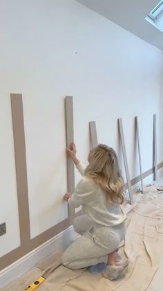 a woman is painting the walls in her house with tape and paint rollers on the floor