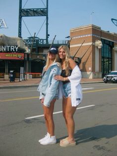 two beautiful young women standing next to each other in front of a baseball field and stadium