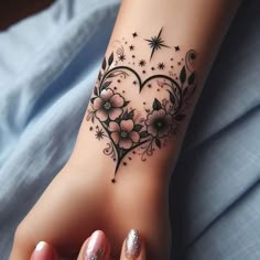 a heart shaped tattoo with flowers and stars on the side of her arm, sitting on top of a bed