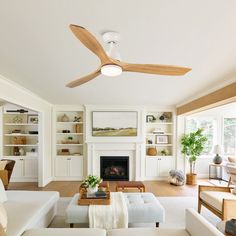 a living room filled with furniture and a fire place under a ceiling fan in front of a fireplace