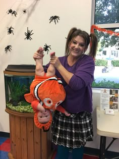 a woman holding an orange stuffed animal in front of a fish tank