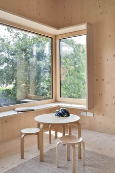 a table and two stools in front of large windows with wood paneled walls