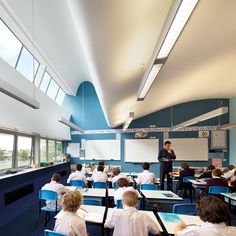 there are many children sitting at desks in the classroom with whiteboards on the wall