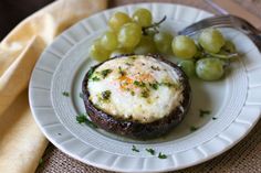 a white plate topped with an egg covered in cheese next to grapes and a fork