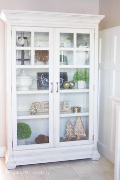 a white china cabinet with glass doors and decorations on the top shelf in front of it