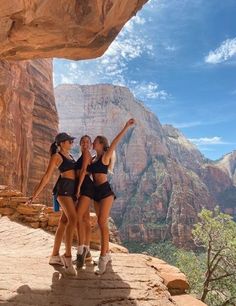 three girls standing on the edge of a cliff with their arms up in the air