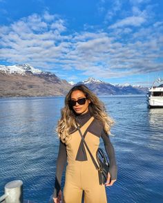 a woman standing on top of a boat in the ocean wearing a body suit and sunglasses