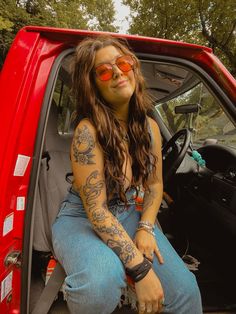 a woman sitting in the back of a red truck with tattoos on her arms and legs