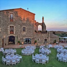 tables and chairs are set outside in front of an old stone building with arches on it