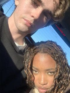 a man and woman with dreadlocks in the back seat of a car looking at the camera