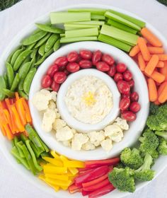 a white plate topped with veggies and dip surrounded by carrots, celery, broccoli