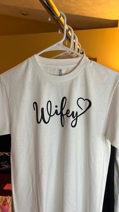 Get ready to rock your wedding with this stunning Wifey Tee! This T-shirt is perfect for any bride or wife-to-be who wants to show off her status in style. Made for women of all sizes, this white T-shirt comes with tags and features the word "Wifey" printed in bold letters, making it an ideal choice for any wedding ceremony or reception.  The tee is available in regular size and can be paired with any bottom of your choice, be it a skirt, jeans, or shorts. The bright white color of the T-shirt is perfect for any occasion, be it a formal or a casual event. Get ready to make a statement with this beautiful Wifey Tee and show off your love in style! White Bridal T-shirt With Short Sleeves, White T-shirt For Bridal Shower Short Sleeve, White Fitted T-shirt For Bachelorette Party, White Short Sleeve T-shirt For Bridal Shower, White Short Sleeve Bride T-shirt, Bride's White Short Sleeve T-shirt, White Short Sleeve Top For Wedding, White Crew Neck Top For Bridal Shower, White Short Sleeve Top For Bridal Shower