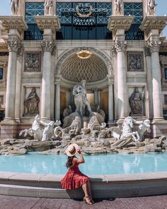 a woman sitting on the edge of a fountain in front of a building with statues