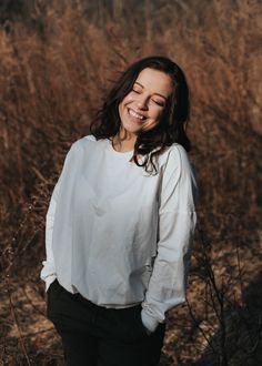 a woman standing in tall grass smiling at the camera