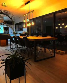 a dining room table and chairs with lights hanging from the ceiling over it, in front of large windows