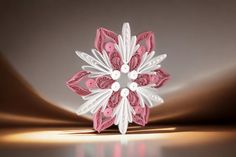 an origami snowflake with pink and white accents on a reflective surface