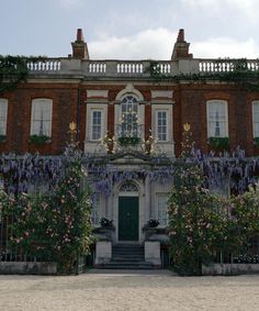 an old brick building with purple flowers growing on it's side and stairs leading up to the front door