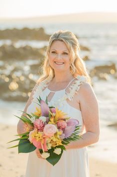 a woman standing on the beach holding a bouquet