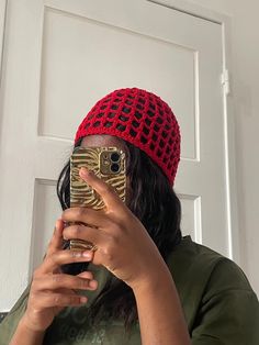 a woman taking a selfie in front of a door wearing a red knitted hat