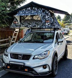 a white car parked in front of a house with a roof tent on it's top