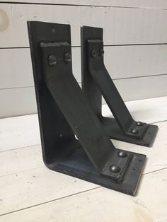 two black metal brackets sitting on top of a wooden floor next to a white wall